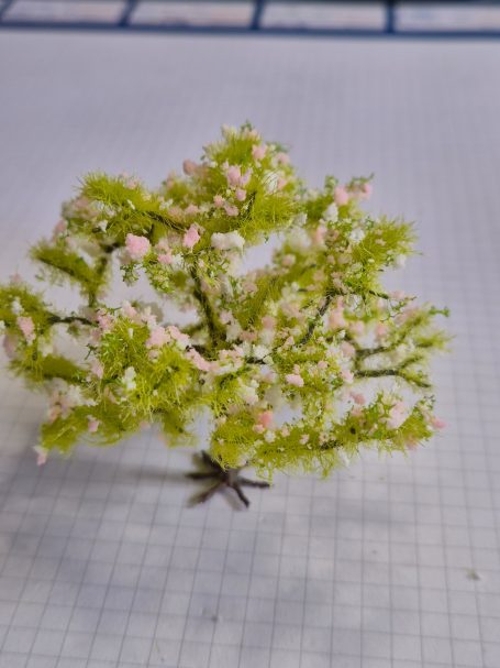 Miniatuurboom met groene bladeren en roze bloemen.