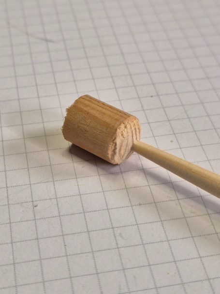 Houten hamer met een rechte steel, op een geruit oppervlak.