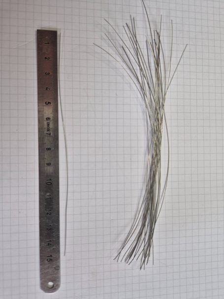 Een metalen liniaal naast een bosje fijne draadjes op een rasterachtergrond.
