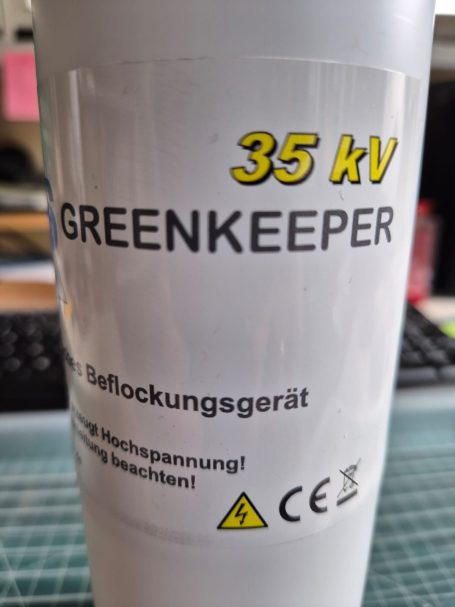 Wit apparaat met tekst "35 kV GREENKEEPER" en waarschuwing symbool.