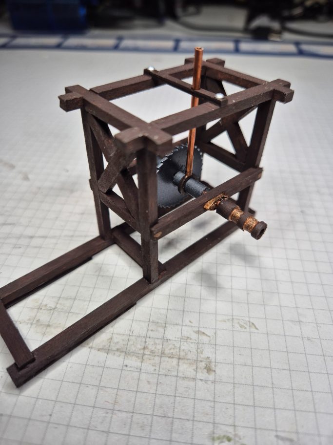 Een bruin houten model van een mechanisme met een motor en een draaischijf.